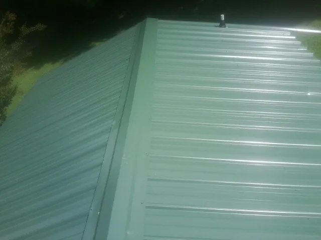 New green metal panels meeting at the ridge of a roof — Flat Roof Repair work by our crew in Hudson